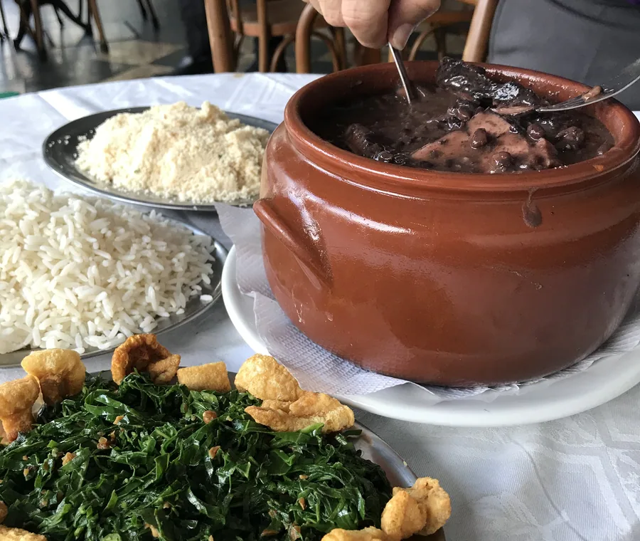 Feijoada do Hera servida na panela de barro com couve, arroz e farofa